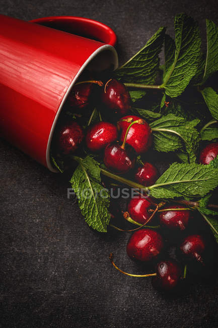 Sabrosas y apetitosas cerezas maduras con hojas que caen de la copa roja en la superficie negra - foto de stock