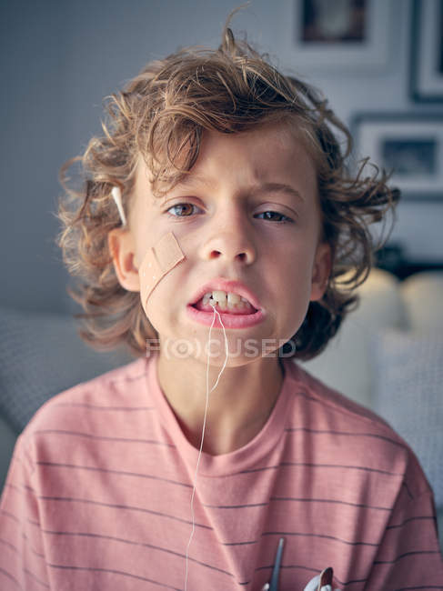 Naughty kid tangling in dental floss making faces while tiring floss to tooth to pull it out looking at camera — Stock Photo