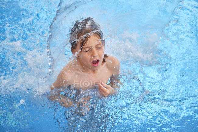 Enfant à la recherche d'air, les yeux fermés et la bouche ouverte lorsqu'il flotte sous une chute dans un parc aquatique — Photo de stock
