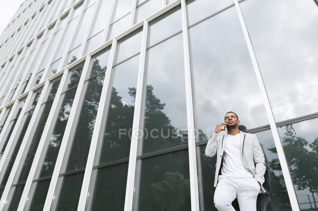 Élégant homme noir parlant avec son smartphone dans un immeuble penché — Photo de stock