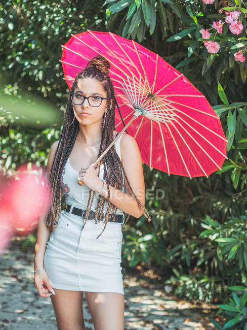 Pensive young woman in summer outfit with umbrella standing in park — Stock Photo