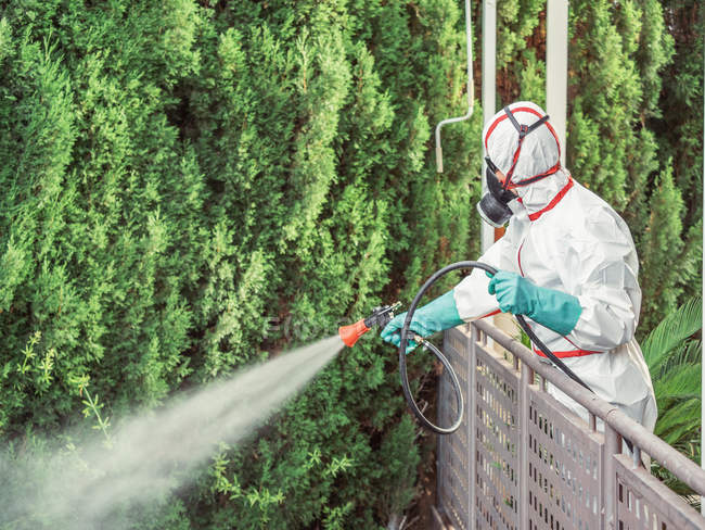 Fumigator in white uniform spraying substance on garden — Stock Photo