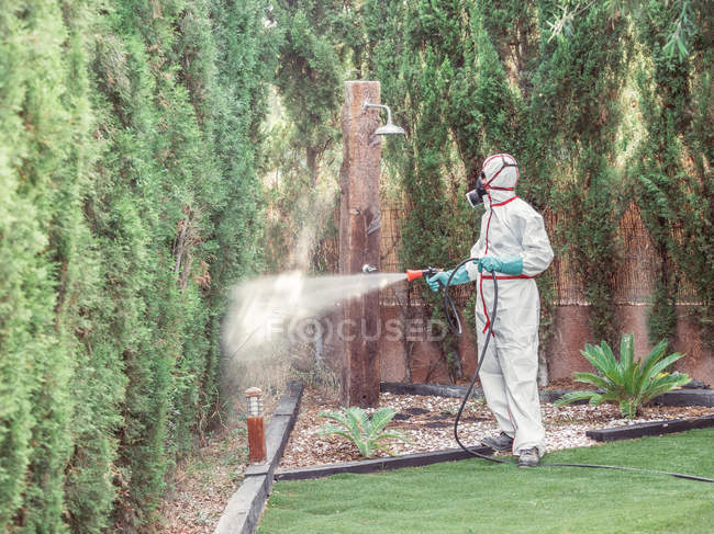 Fumigateur en blanc uniforme pulvérisation substance sur le jardin — Photo de stock