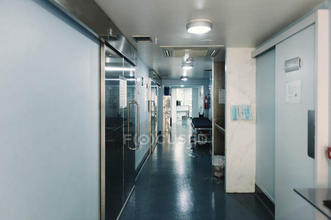 Deserted corridor in clinic with empty hospital trolley and lights on — Stock Photo