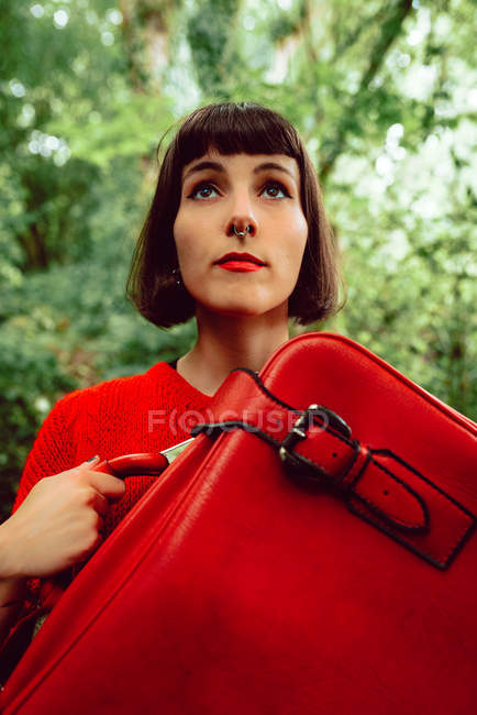 Woman in red with big red suitcase walking in green forest — Stock Photo