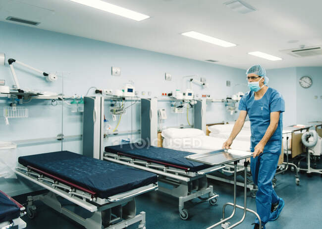 Sanitäter in blauer Uniform und Schutzmaske stellen Tablett auf Trolley im Krankenhauszimmer vor leeren Betten auf — Stockfoto
