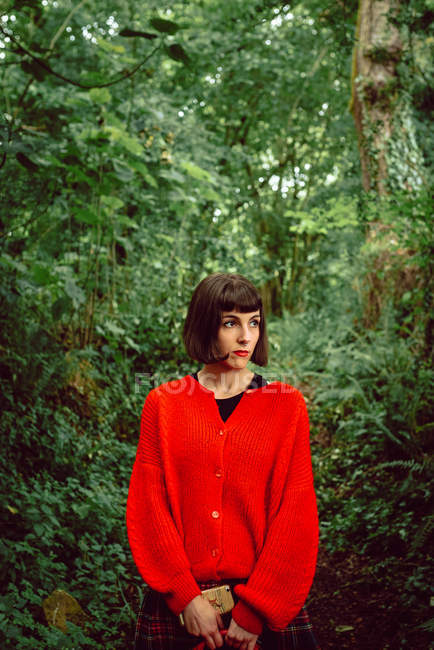 Woman in red with red suitcase walking in green forest — Stock Photo