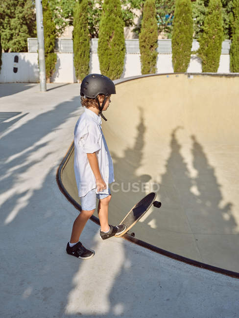 Vista lateral do menino vestindo capacete protetor e andar de skate na rampa no parque de skate — Fotografia de Stock