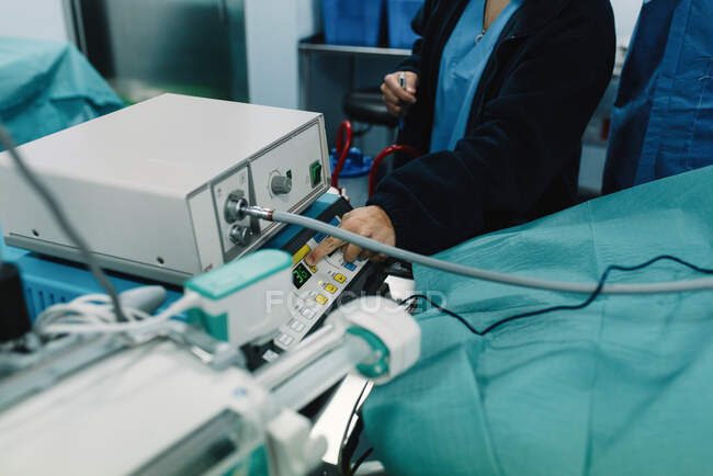 From above crop doctor pressing button on medical equipment connected to patient lying in intensive care unit — Stock Photo