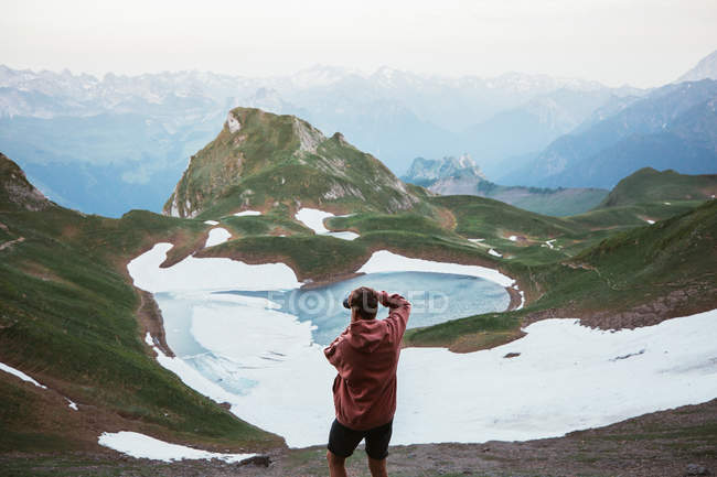 Back view of male tourist taking photo of mountain lake surrounded by snow and ridge in Pyrenees — Stock Photo