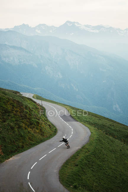 Dall'alto vista di mattina di montagne di Pirenei nebbiose e skateboard di viaggiatore maschile su serpentine — Foto stock
