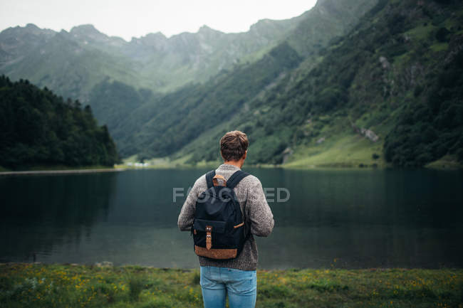 Back view of male tourist with backpack enjoying Pyrenees mountains and clear lake — Stock Photo