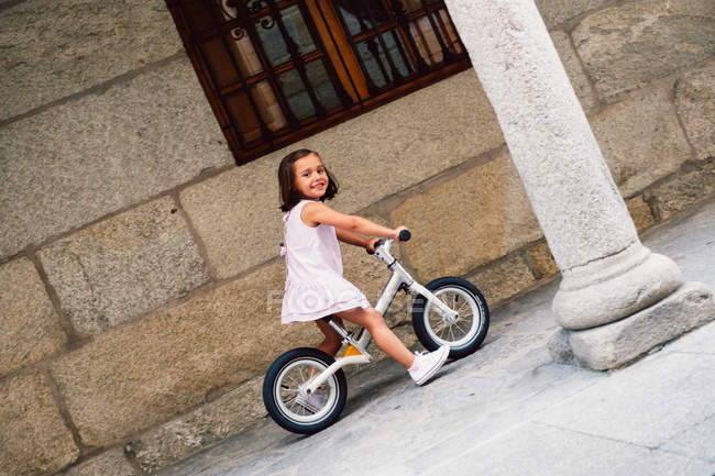 На старовинній вулиці між колонами зображено веселу дівчину, яка їде на маленькому велосипеді. — стокове фото