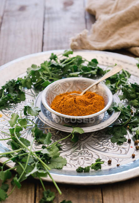 From above friable yellow turmeric in mug and greens on round silver plate on wooden table — Stock Photo