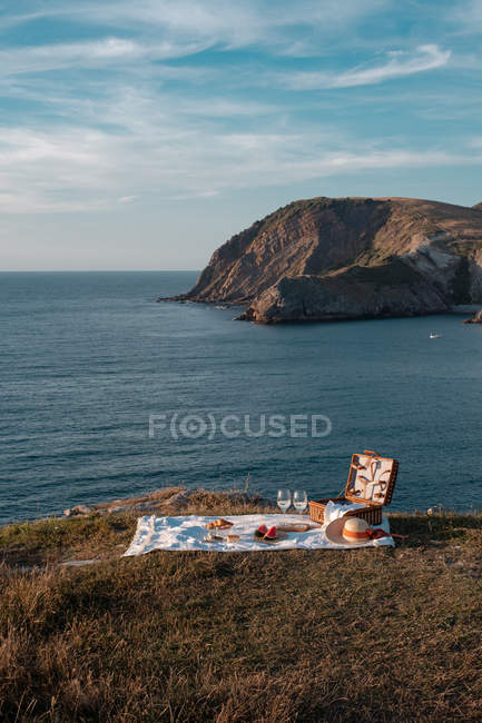 Esterilla de picnic con romántico conjunto con vasos de bebida y comida en la costa rocosa del mar - foto de stock