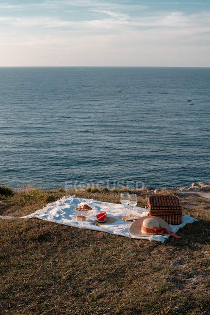Tapis de pique-nique avec ensemble romantique avec des verres de boisson et de nourriture sur le rivage de la mer rocheuse — Photo de stock
