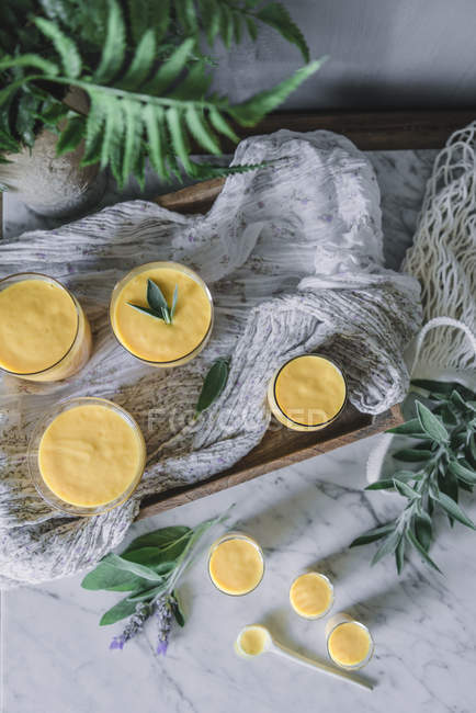 Tasty aromatic mango mousse in glass mugs and spoon on table decorated with green plants — Stock Photo