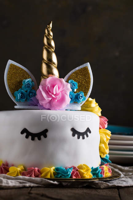 Bonito pastel de unicornio con ojos cerrados pintados en mesa de madera sobre fondo oscuro - foto de stock