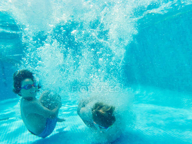 Cheerful playful boys jumping deep inside of clear pool water having fun — Stock Photo