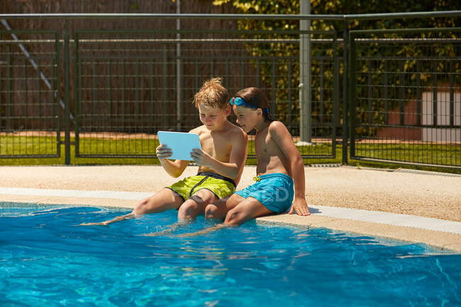 Chicos en la tableta de navegación junto a la piscina - foto de stock