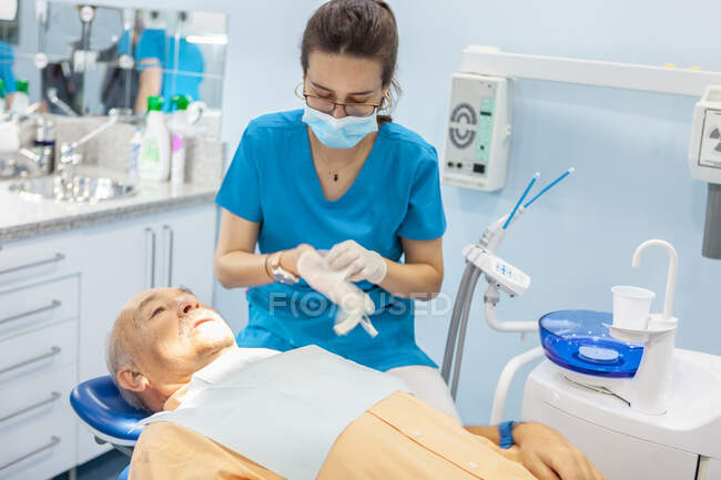 Dentist putting on surgical gloves while patient lying in chair — Stock Photo