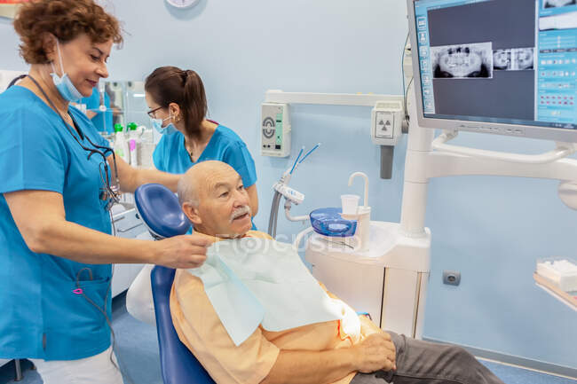 Dentiste mettre du tissu sur la poitrine au patient dans la chaise — Photo de stock