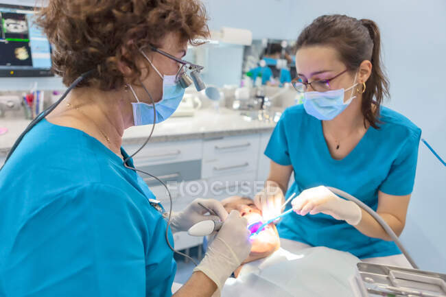 Dentisti in maschera mettendo sigillo in bocca aperta del paziente in sedia — Foto stock