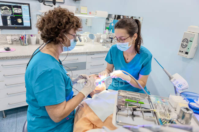 Dentistas em máscara colocando selo na boca aberta do paciente em cadeira — Fotografia de Stock