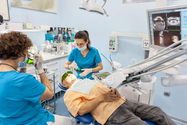 Dentistas en máscara poniendo sello en la boca abierta del paciente en silla - foto de stock