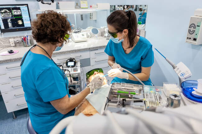 De arriba paciente maduro acostado en la silla mientras que especialista calificado en uniforme y gafas que preparan para la inspección usando guantes del cirujano - foto de stock