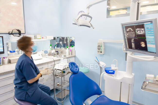 Silla vacía y dentista mirando al monitor con imagen de dientes - foto de stock