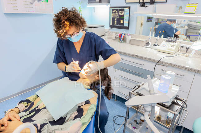 From above confident specialist in surgical gloves making injection with syringe and working with dental tools in mouth of patient lying under bright light in chair in cabinet — Stock Photo