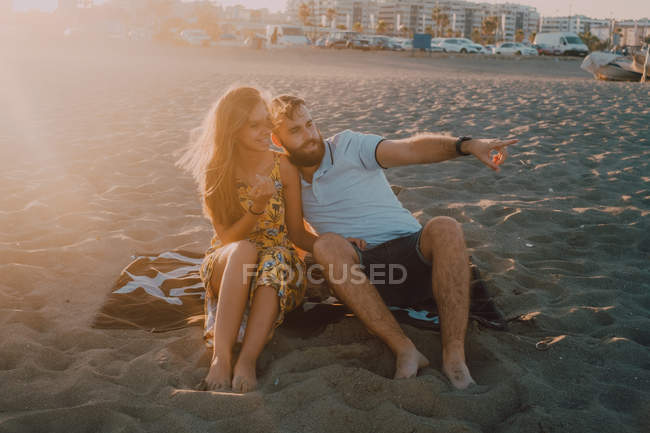 Pareja joven enamorada apuntando en la playa en la romántica puesta del sol - foto de stock
