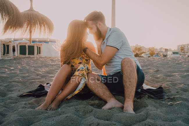 Jóvenes enamorados ligándose en la playa en la romántica noche de atardecer - foto de stock
