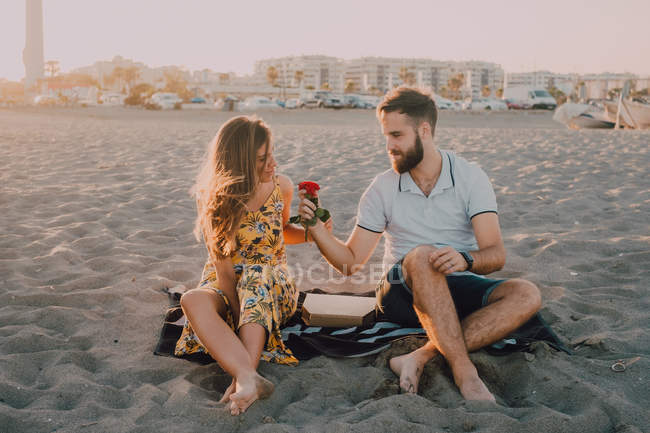 Amorous man giving charming woman rose on beach at sunset evening — Stock Photo