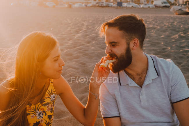 Homem amoroso barbudo e mulher de cabelos compridos alimentando-se uns aos outros com ternura à luz solar — Fotografia de Stock