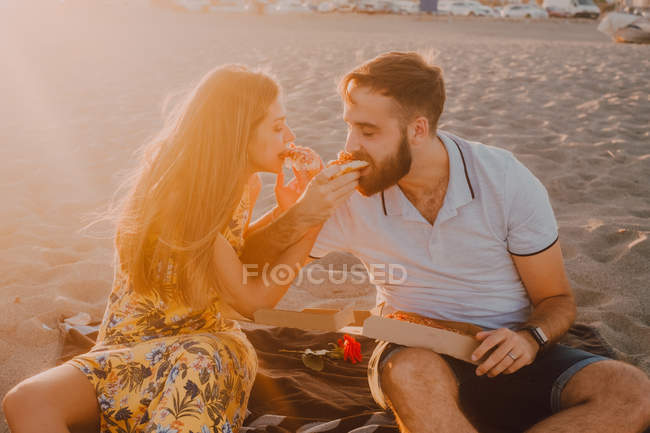 Homem amoroso barbudo e mulher de cabelos longos alimentando-se uns aos outros com ternura à luz do sol — Fotografia de Stock