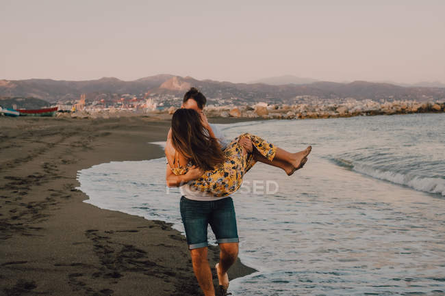 Langhaarige Frau im Arm eines Mannes, der im schäumenden Wasser am Meer spaziert — Stockfoto