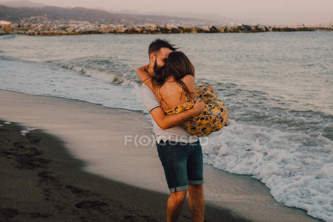 Long-haired woman in arms of man walking in foamy water seaside — Stock Photo