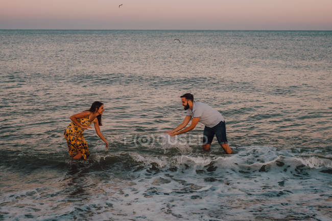Amorous young people splashing and playing in water under serene sky with seagull — Stock Photo