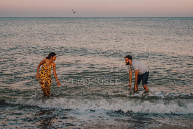 Verliebte junge Leute planschen und spielen im Wasser unter heiterem Himmel mit Möwe — Stockfoto