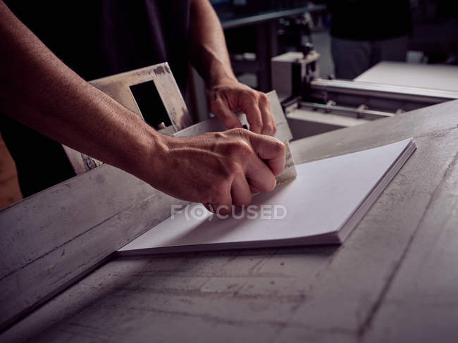 Unrecognizable bookbinder working with sheets of paper on special equipment in printing office — Stock Photo