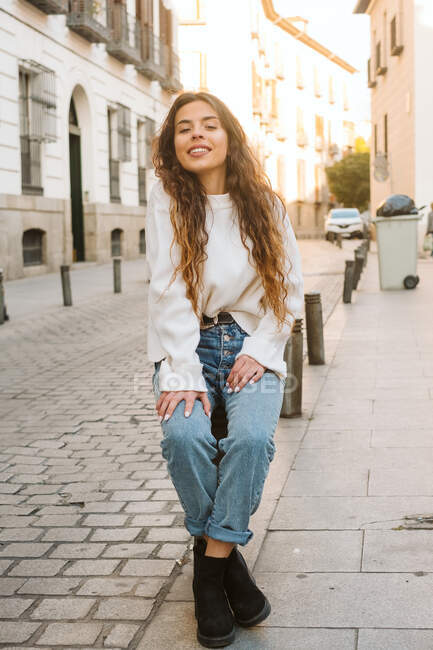 Pretty young female in casual outfit smiling and looking at camera on sunny day in city street — Stock Photo