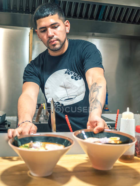 Jovem de t-shirt preta colocando tigelas de mesa de prato japonês cozido fresco chamado ramen — Fotografia de Stock