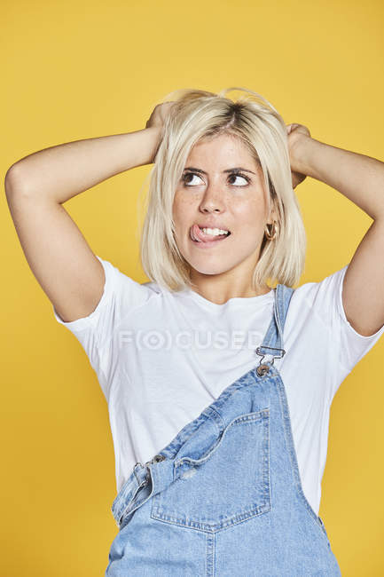 Belle jeune femme en t-shirt blanc et jean sundress debout sur fond jaune et levant les yeux — Photo de stock