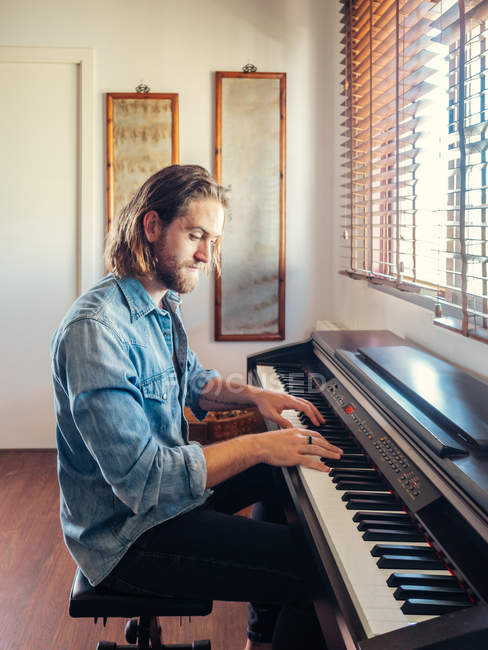 Життєрадісний молодий чоловік грає синтезатор за вікном в квартирі — стокове фото