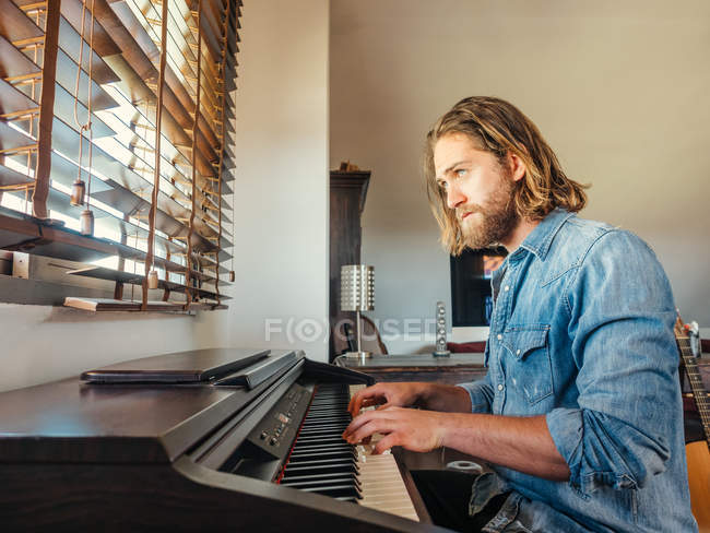 Pensive man composing melody on electronic piano in apartment — Stock Photo