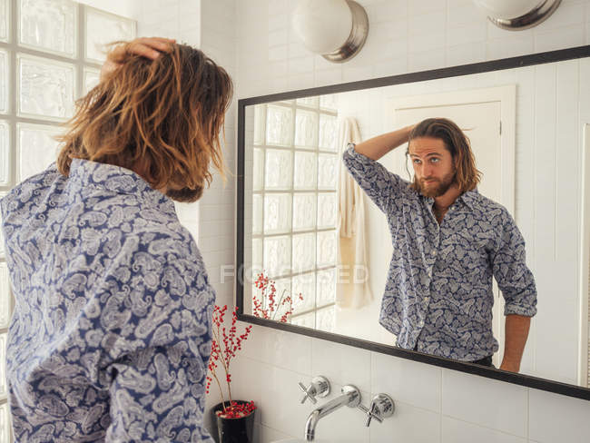 Красивый молодой человек проверяет прическу в зеркальном отражении — стоковое фото