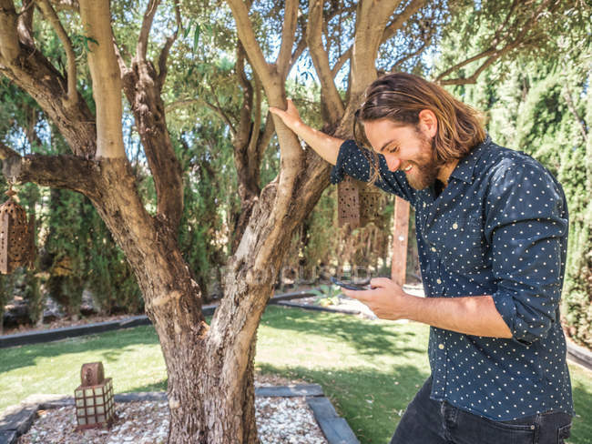 Schöner junger Mann mit Handy im Garten — Stockfoto