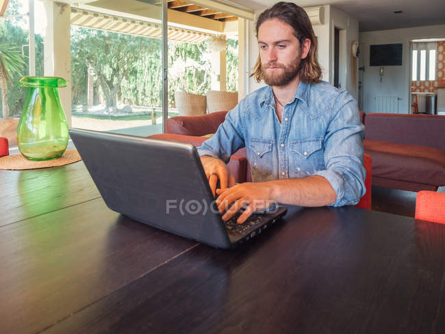 Hombre enfocado usando computadora en apartamento - foto de stock
